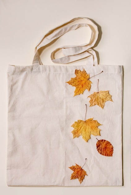 Concepto de venta de otoño. Etiquetas de cartón con porcentajes, hojas de otoño amarillas en bolsa de compras de lino ecológico sobre superficie beige. Endecha plana.
