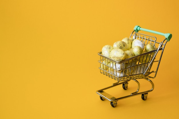 Concepto de venta de Pascua. Huevos de Pascua amarillos en carrito de la compra pequeño en amarillo.