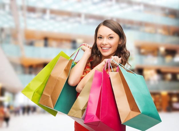 concepto de venta, regalos, vacaciones y personas - mujer sonriente con bolsas coloridas sobre el fondo del centro comercial