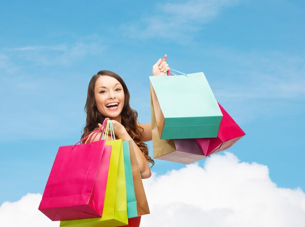 concepto de venta, regalos, vacaciones y personas - mujer sonriente con coloridas bolsas de compras sobre cielo azul y fondo de nube blanca