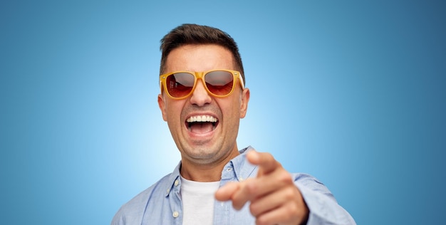 concepto de verano, estilo, emociones y personas - cara de un hombre latino de mediana edad que se ríe con camisa y gafas de sol sobre fondo azul