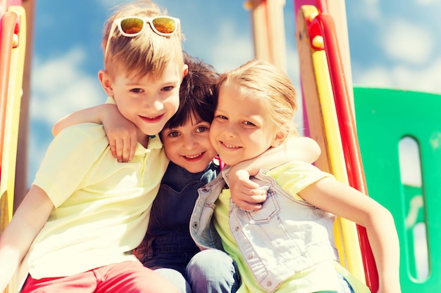 concepto de verano, infancia, ocio, amistad y personas - grupo de niños felices abrazándose en el parque infantil