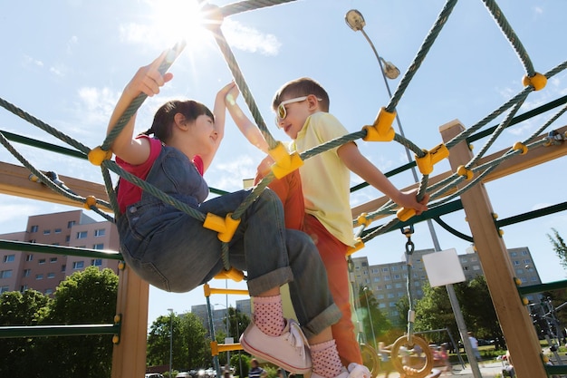 concepto de verano, infancia, ocio, amistad y personas - grupo de niños felices en el parque infantil de escalada