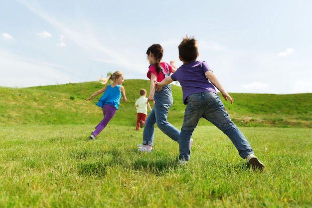 concepto de verano, infancia, ocio y personas - grupo de niños felices jugando al juego de etiquetas y corriendo en el campo verde al aire libre