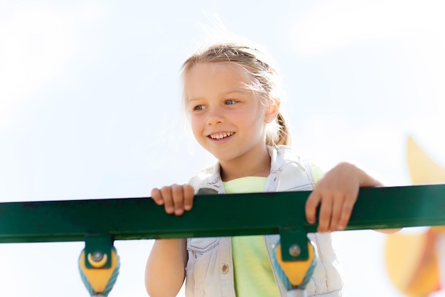 concepto de verano, infancia, ocio y personas - niñita feliz en el marco de escalada del parque infantil