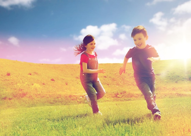 concepto de verano, infancia, ocio y personas - niño y niña felices jugando al juego de etiqueta y corriendo al aire libre en un campo verde