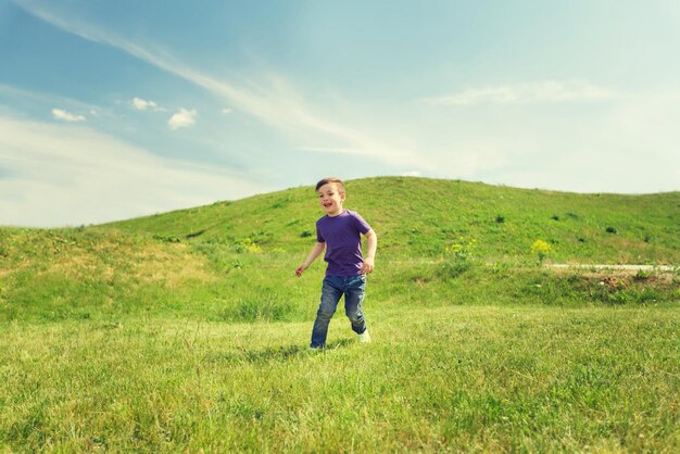 concepto de verano, infancia, ocio y personas - niño pequeño feliz corriendo en el campo verde al aire libre