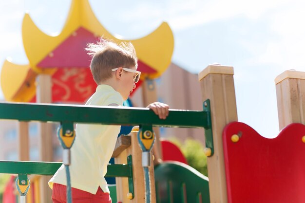 concepto de verano, infancia, ocio y personas - niño pequeño feliz en el parque infantil de escalada