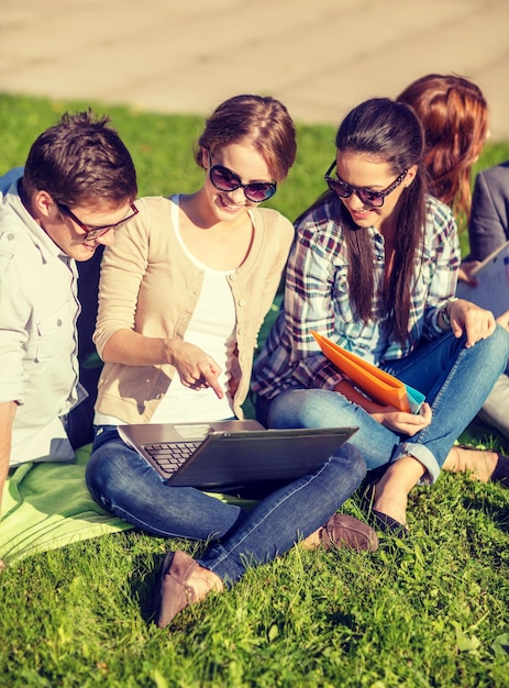 concepto de verano, internet, educación, tecnología y campus - grupo de estudiantes o adolescentes con laptop, cuadernos y carpetas