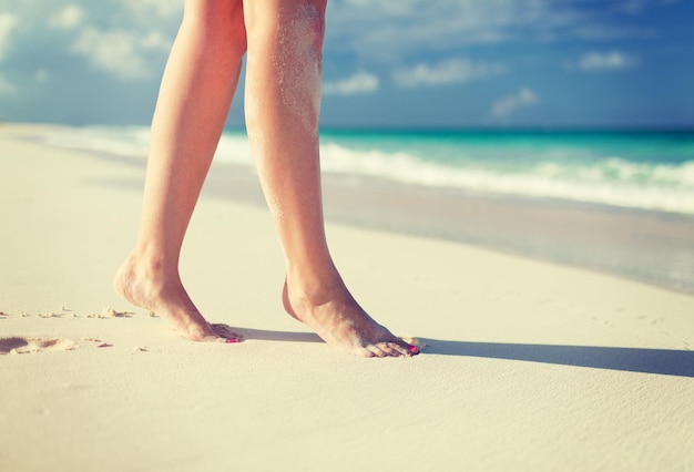 concepto de verano, playa, ocio y parte del cuerpo - primer plano de las piernas de la mujer en la orilla del mar