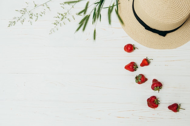 Concepto de verano, sombrero de paja, fresas frescas y tallos de hierba sobre un fondo de madera