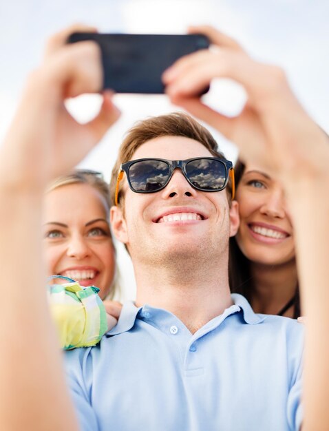 concepto de verano, vacaciones, vacaciones y felicidad - grupo de amigos tomando fotografías con el teléfono inteligente