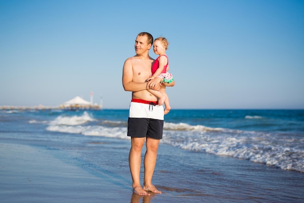 Concepto de verano y viajes - retrato de padre joven feliz con hija pequeña en la playa