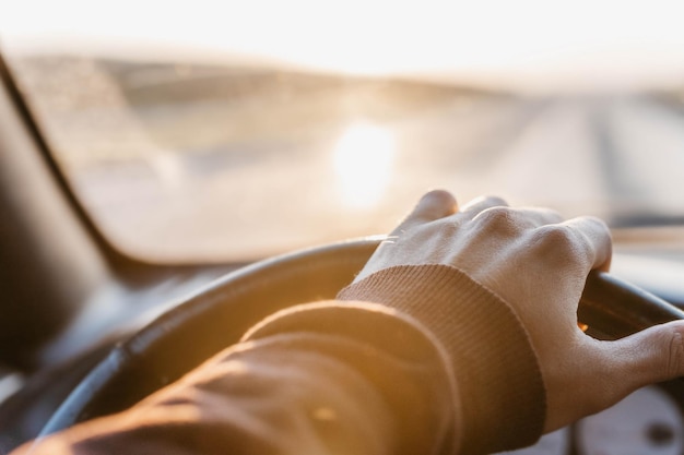 concepto de viajar en coche la mano del conductor en el volante al atardecer