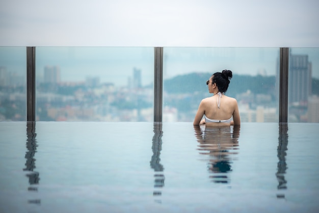 Concepto de viaje asiático. Mujer joven disfrutando de la vista del cielo de la ciudad desde la piscina de la azotea del hotel, estilo de vida de niña hermosa al aire libre en tiempo de vacaciones