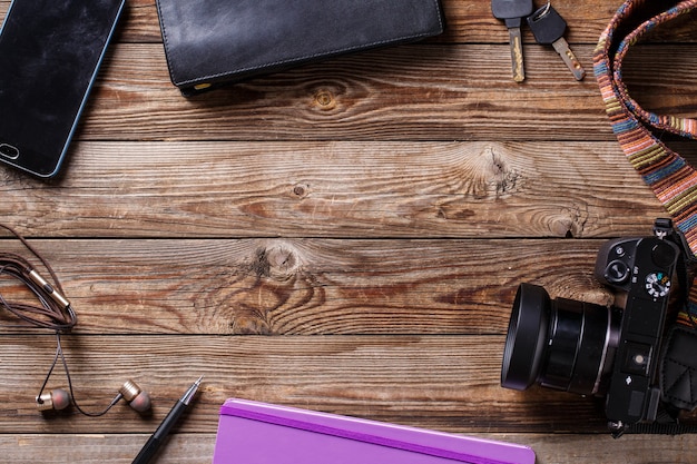 Concepto de viaje: auriculares, cámara, cuaderno de bocetos, bolso, lápiz y llaves sobre fondo de madera. Foto de vista superior plana con copyspace en el centro.