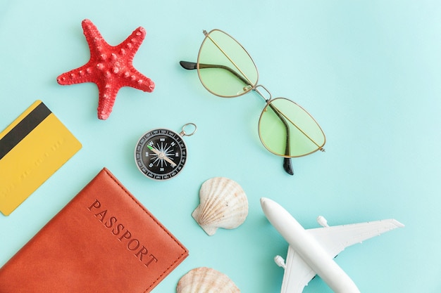 Concepto de viaje de aventura de viajes de vacaciones. Mínimo plano simple con pasaporte plano, gafas de sol, brújula, carcasa de tarjeta de crédito dorada sobre fondo azul pastel colorido de moda.
