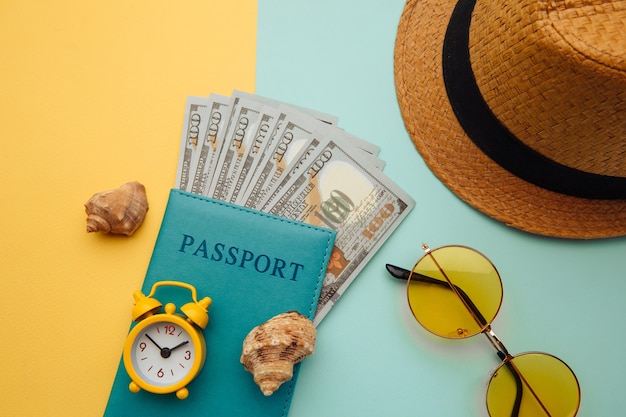 Concepto de viaje de aventura de viajes de vacaciones. Plano mínimo simple con sombrero, pasaporte y concha sobre superficie azul amarillo. Esenciales turísticos