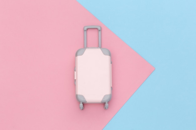 Concepto de viaje. Mini maleta de viaje de plástico sobre fondo rosa pastel azul. Estilo minimalista. Vista superior, endecha plana