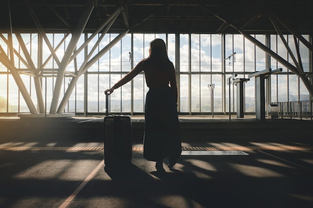 Concepto de viaje Mujer joven que espera con la maleta en la plataforma en la estación de tren