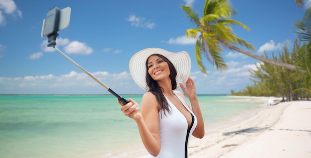 concepto de viaje, ocio, verano, tecnología y personas - mujer joven sexy tomando selfie con teléfono inteligente en el fondo de la playa tropical