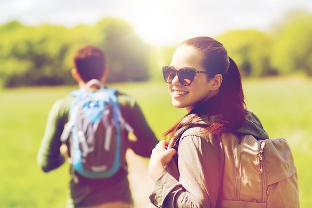 concepto de viaje, senderismo, mochilero, turismo y personas - pareja feliz con mochilas caminando por la carretera rural al aire libre