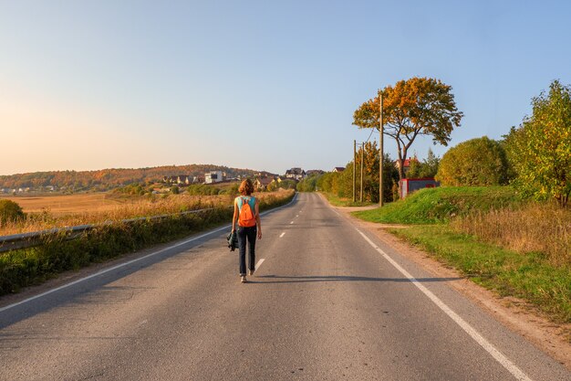 Concepto de viaje en solitario. Vista posterior de la mujer con mochila caminando por la carretera de otoño, excursión.