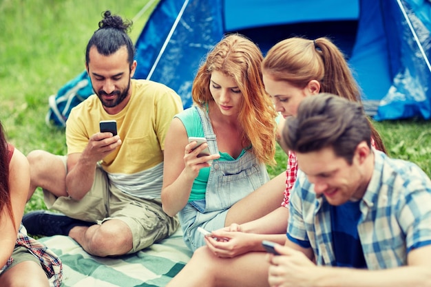 concepto de viaje, turismo, caminata, tecnología y personas - grupo de amigos con smartphone y carpa en el campamento