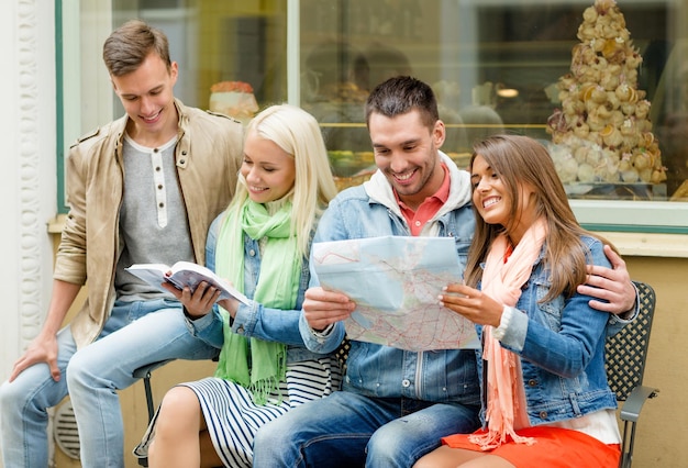 concepto de viaje, vacaciones y amistad - grupo de amigos sonrientes con guía de la ciudad y mapa explorando la ciudad