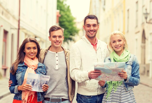 concepto de viaje, vacaciones y amistad - grupo de amigos sonrientes con guía de la ciudad y mapa explorando la ciudad