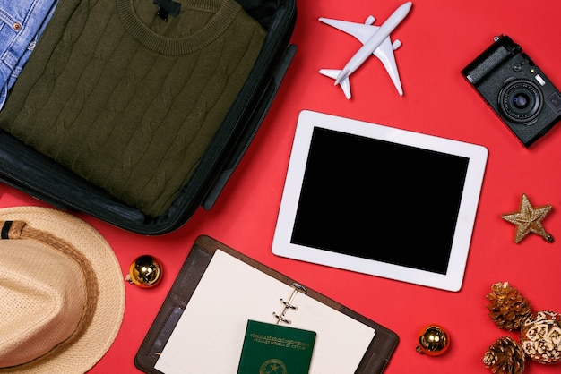 Concepto de viaje de vacaciones: pasaporte, cámara, sombrero, avión, decoraciones navideñas sobre fondo rojo.