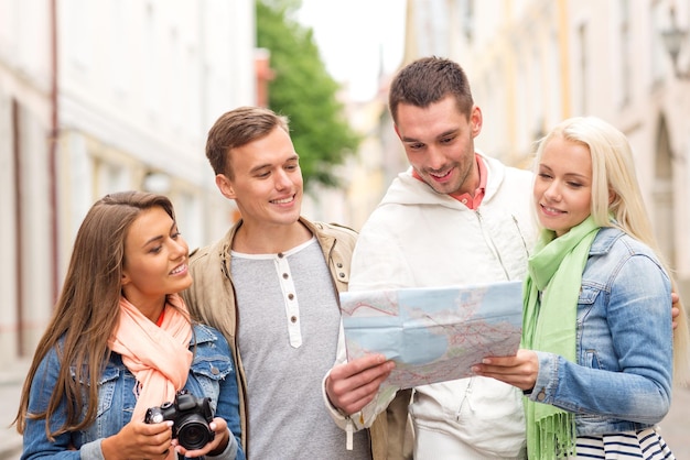 concepto de viaje, vacaciones, tecnología y amistad - grupo de amigos sonrientes con mapa y cámara fotográfica explorando la ciudad