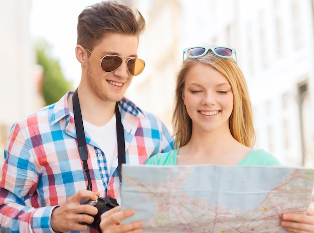 concepto de viaje, vacaciones, tecnología y amistad - pareja sonriente con mapa y cámara fotográfica explorando la ciudad