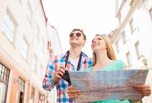 Foto concepto de viaje, vacaciones, tecnología y amistad - pareja sonriente con mapa y cámara fotográfica explorando la ciudad