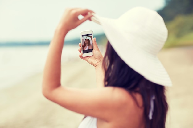 concepto de viaje, verano, tecnología y personas - mujer joven sexy tomando selfie con teléfono inteligente en la playa