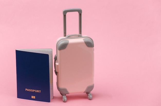 Concepto de viajes internacionales. Mini maleta de viaje de plástico con pasaporte sobre fondo rosa.