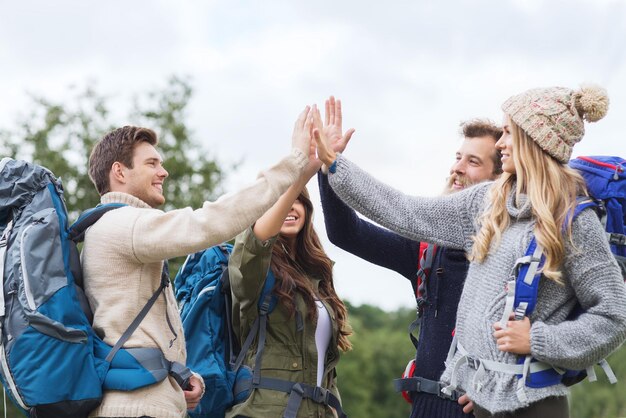 concepto de viajes, turismo, caminatas, gestos y personas - grupo de amigos sonrientes con mochilas haciendo cinco al aire libre