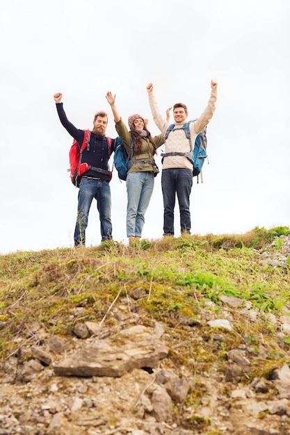 concepto de viajes, turismo, caminatas, gestos y personas - grupo de amigos sonrientes con mochilas levantando la mano al aire libre