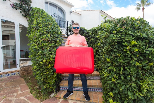 Concepto de viajes, turismo y personas. un joven parado en la escalera con una maleta roja en la mano y sonriendo.