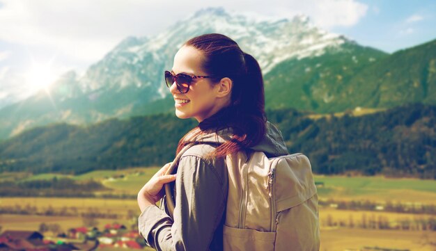 Concepto de viajes, turismo y personas: mujer joven feliz con mochila sobre el fondo de las montañas de los Alpes