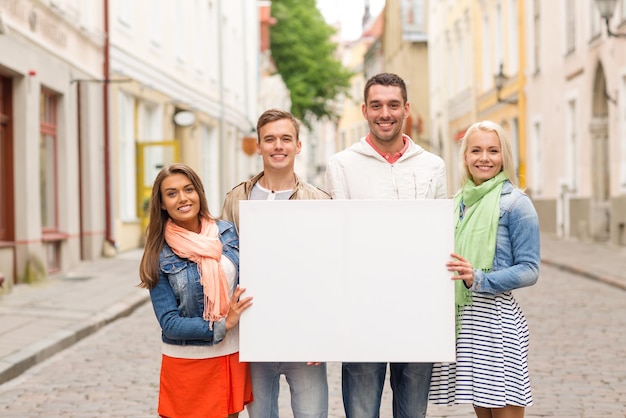 concepto de viajes, vacaciones y publicidad - grupo de amigos sonrientes con pizarra en blanco en la ciudad