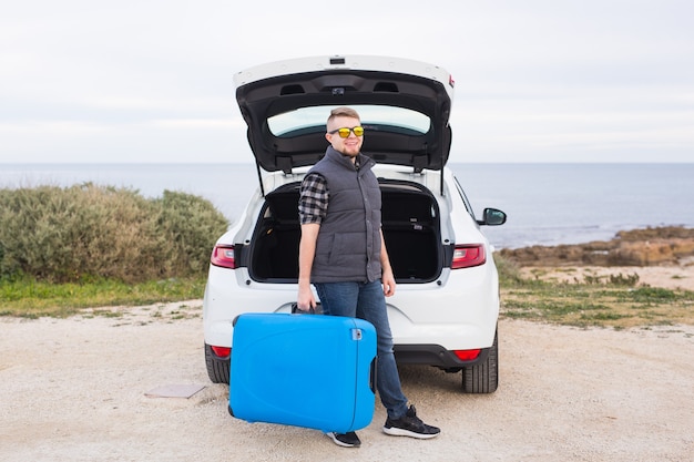 Concepto de viajes, vacaciones y vacaciones. hombre cerca del coche con maleta azul.