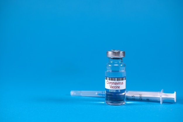 Foto concepto de victoria sobre la epidemia del virus sarsncov ncov derrotado inventó la vacuna covid de coronavirus en un frasco de medicina de vidrio jeringa para inyección sobre fondo azul con espacio para texto