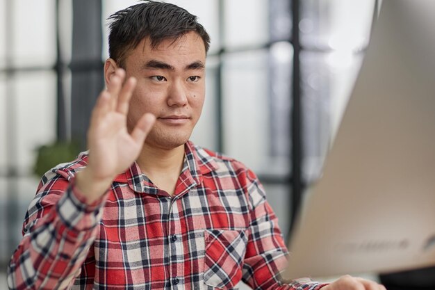 Concepto de videollamada de reunión virtual Hombre multirracial alegre con ropa informal usando una computadora portátil de moda para videollamadas saludando con la mano a su diverso equipo