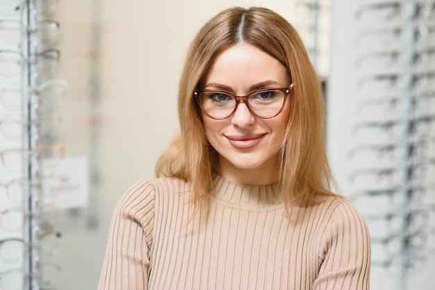 Concepto de visión y visión - mujer de negocios joven que elige gafas en la tienda de óptica