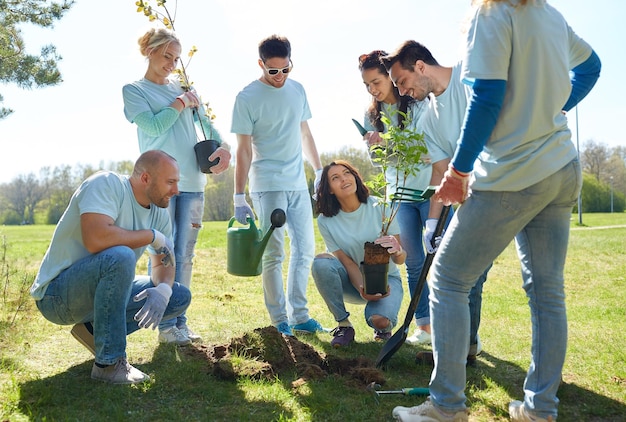 concepto de voluntariado, caridad, personas y ecología - grupo de voluntarios felices plantando árboles y cavando agujeros con pala en el parque