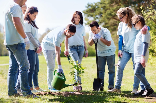 concepto de voluntariado, caridad, personas y ecología - grupo de voluntarios felices plantando y regando árboles con lata en el parque