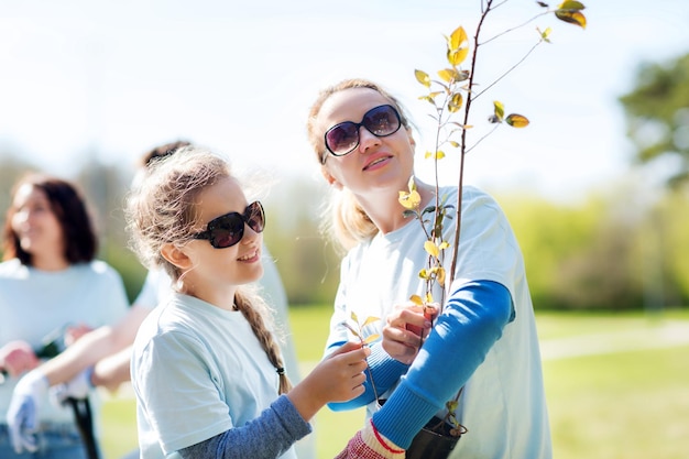 concepto de voluntariado, caridad, personas, familia y ecología - madre e hija voluntarias con plántulas de árboles en el parque