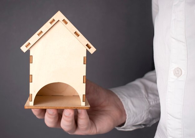 Conceptos de construcción. Mano sosteniendo una casa en miniatura de madera, la mano del hombre sostiene simbólicamente una mini casa de madera