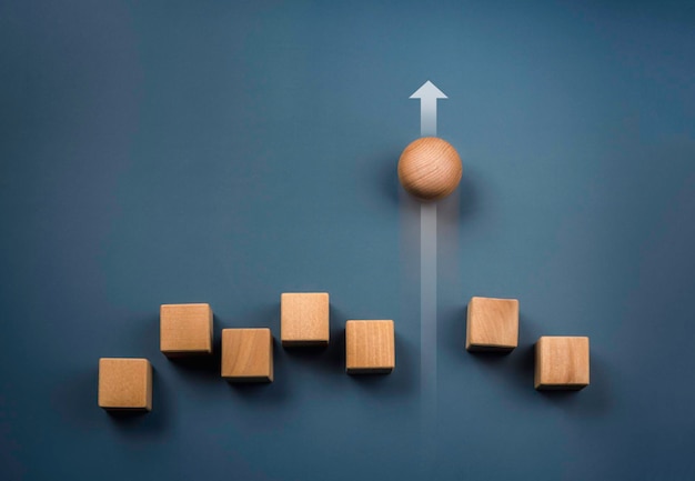 Conceptos de liderazgo, éxito empresarial, singularidad, diferencia, desafío y motivación. Esfera de madera rodando más rápido liderando con flecha ascendente y siguiendo con bloques de cubos de madera sobre fondo azul.